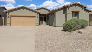 A residential building with a garage, a covered patio, and a gravel driveway. - Spacious 4-bedroom house in welcoming Goodyear with Dual AC and Pool (Goodyear)