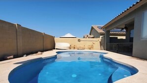 A swimming pool with a curved edge, surrounded by a concrete deck and a brick wall. - Spacious 4-bedroom house in welcoming Goodyear with Dual AC and Pool (Goodyear)