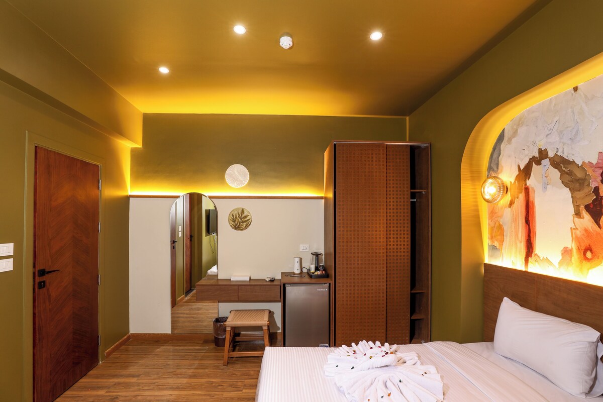 A hotel room with a bed, a desk, a mirror, and a wall-mounted artwork.