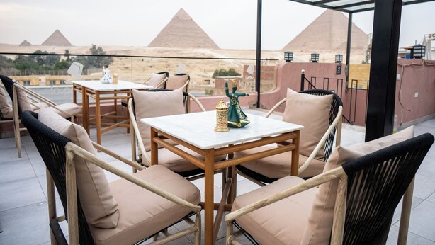 Eine Terrasse mit Korbstühlen und Tischen, mit Blick auf Pyramiden.