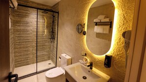 Ein modernes Badezimmer mit einer gläsernen Duschkabine, Toilette, Waschbecken und einem Spiegel mit integrierter Beleuchtung.