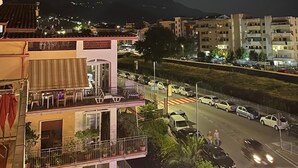 A nighttime view of a building with a balcony, a street with cars, and mountains in the background. - Cozy Double Room with Sea and Mountain view Terrace (Diamante)