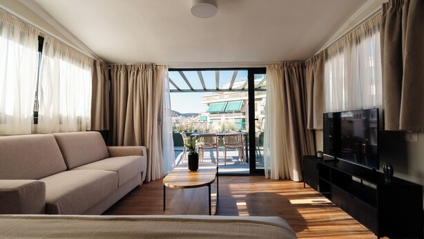 A hotel room with a sofa, a TV, a small table with a plant, and a balcony with outdoor furniture. - The Verve by Zoia Living (Athens)