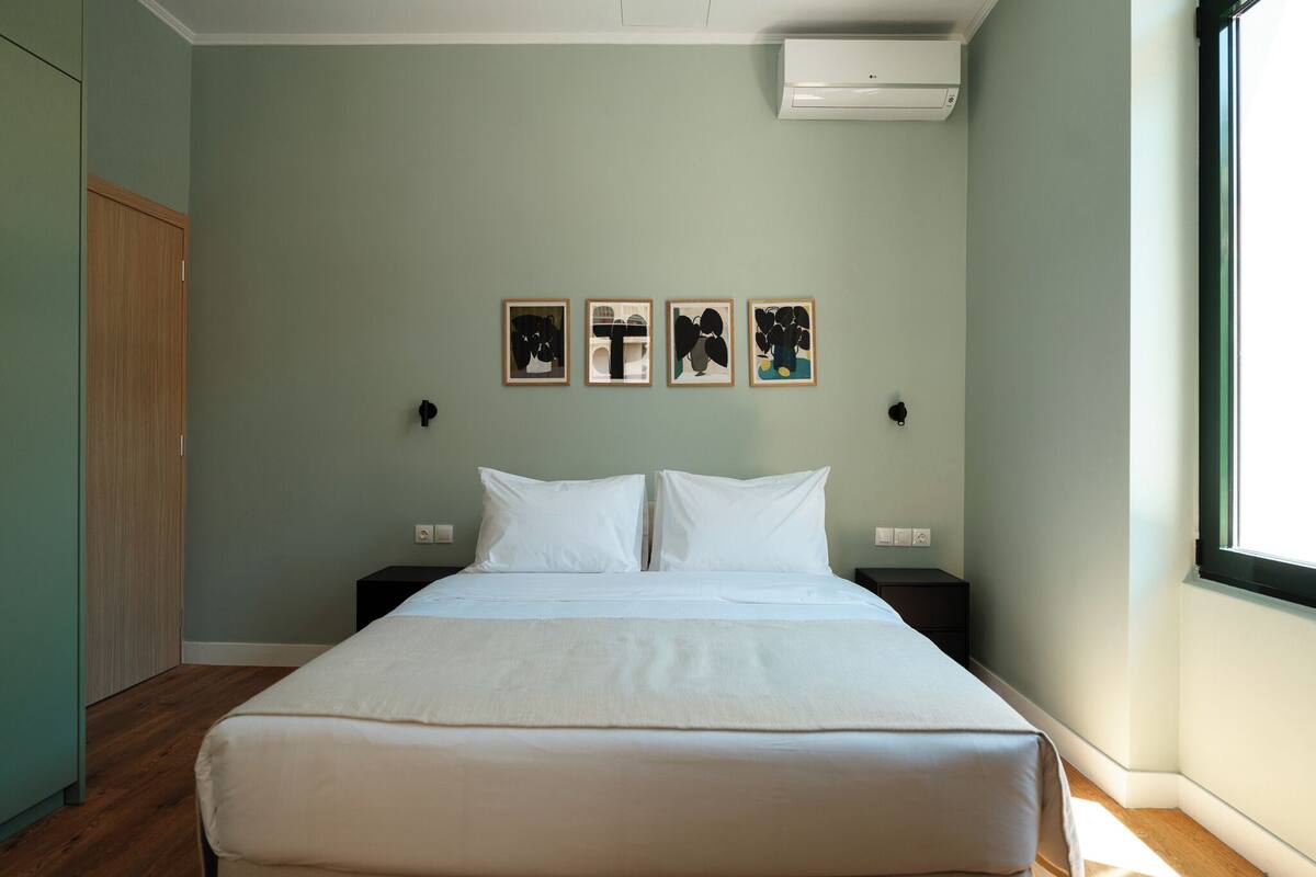 A bedroom with a bed, two bedside tables, a wardrobe, and four framed artworks on the wall.