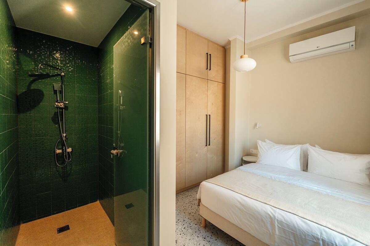 A modern bedroom with a large bed, a walk-in closet, and a shower area with green tiles.