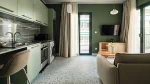 A modern kitchen with a marble backsplash, a sink, and a washing machine. There is a dining area with a table and chairs, and a TV mounted on the wall. - The Verve by Zoia Living (Athens)