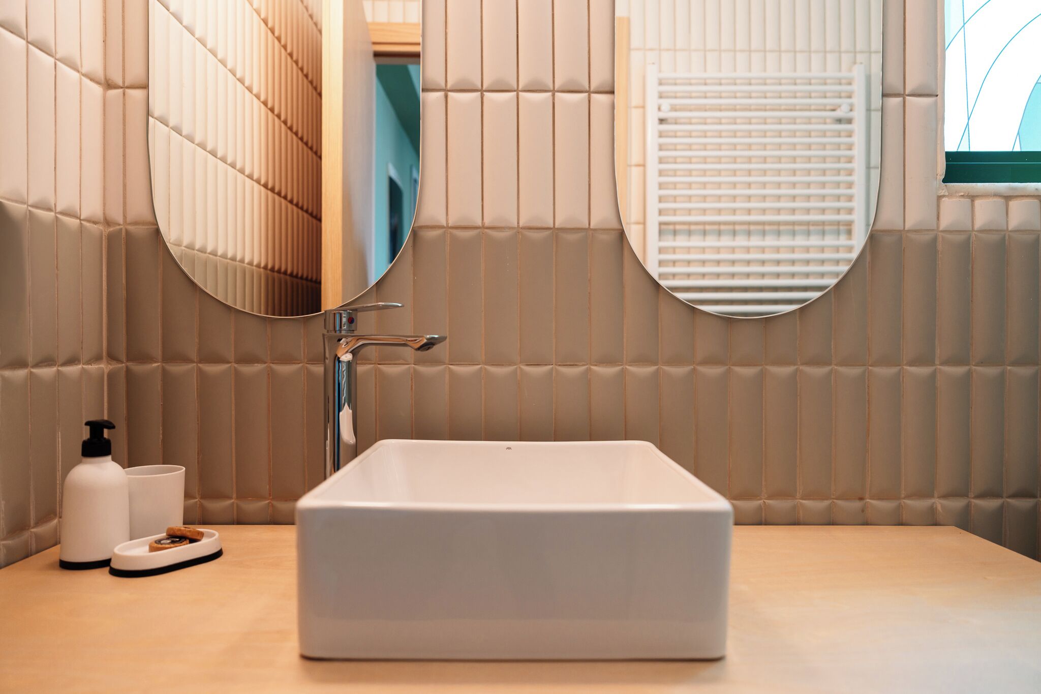 Une salle de bain avec un lavabo rectangulaire, un miroir et une fenêtre avec des stores.