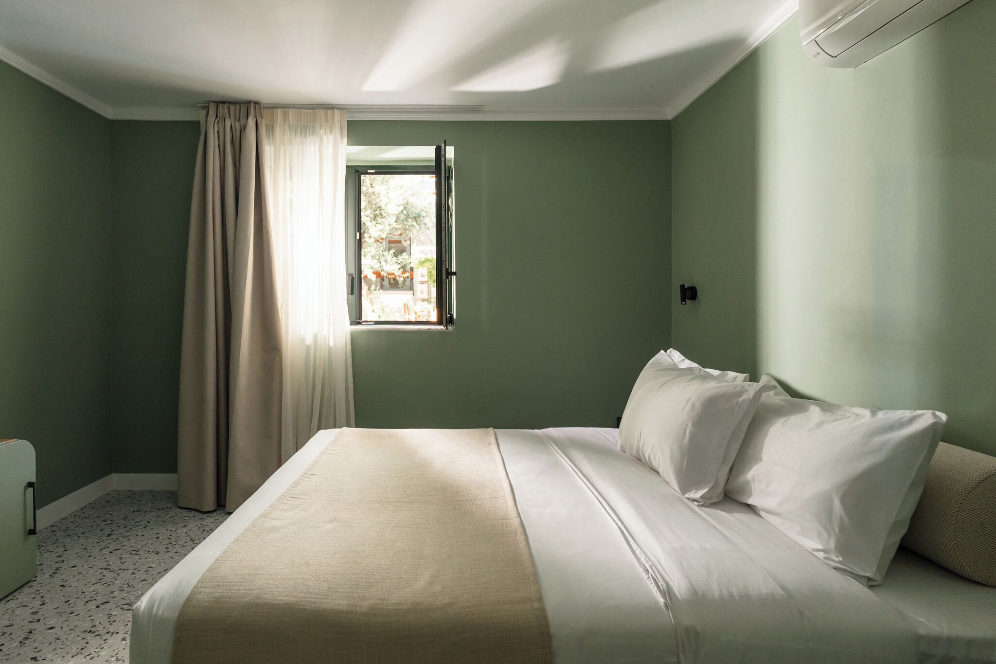 Quarto com cama, janela com cortinas e radiador.