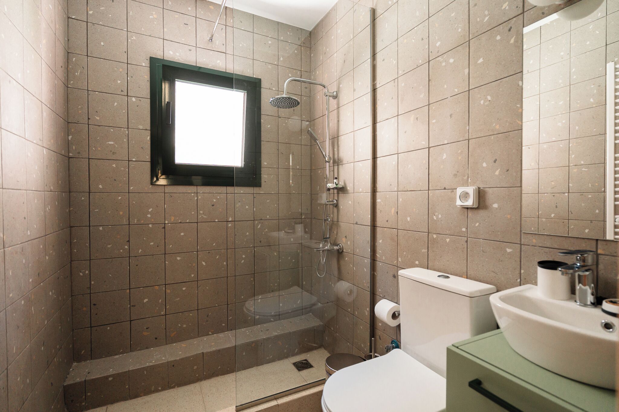 A bathroom with a shower, toilet, sink, and a window.