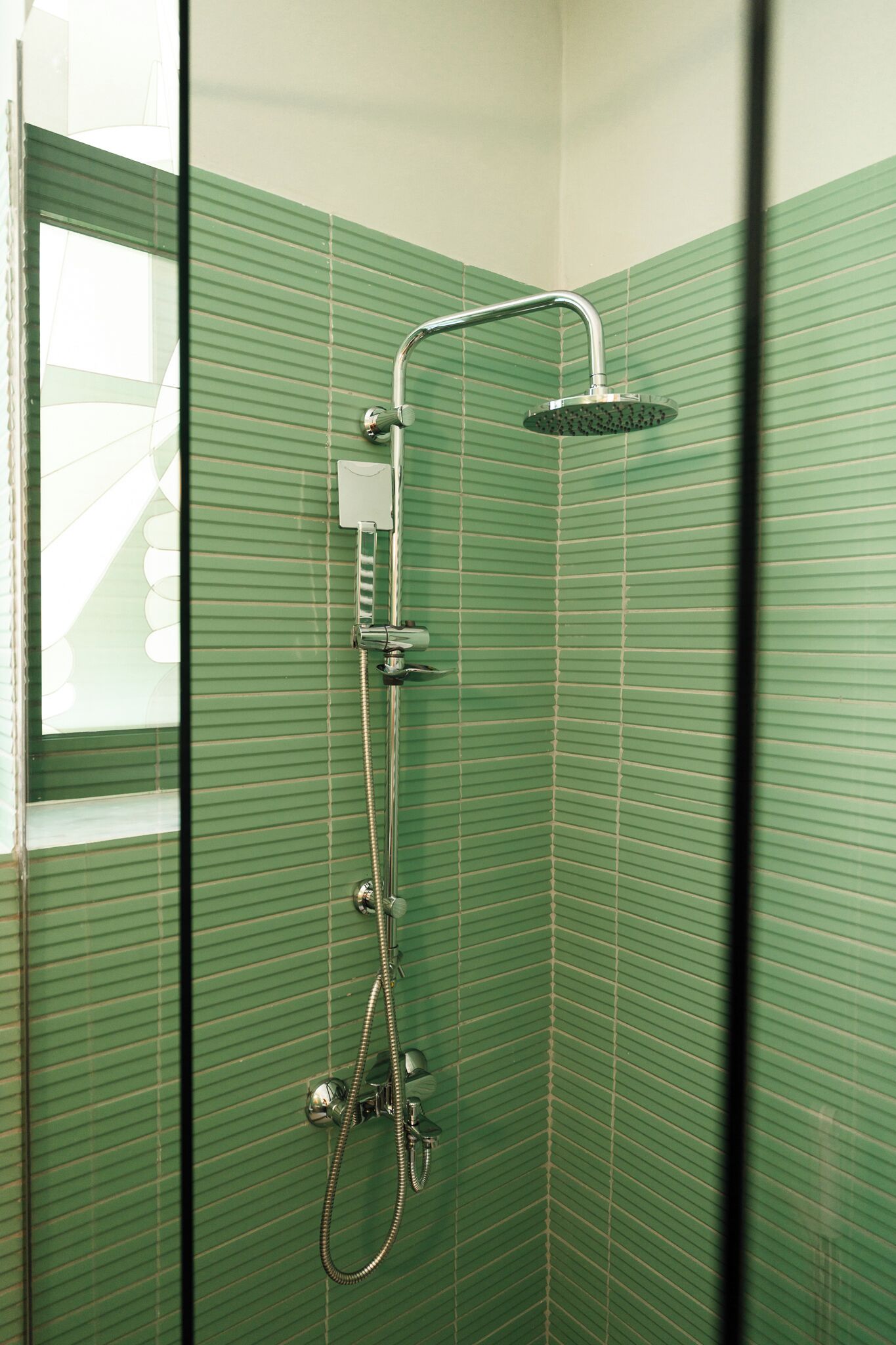 Een douche met een handdouche en een vastgeplaatste douchekop, beide bevestigd aan een muur met een groen, ribbelpatroon van tegels.