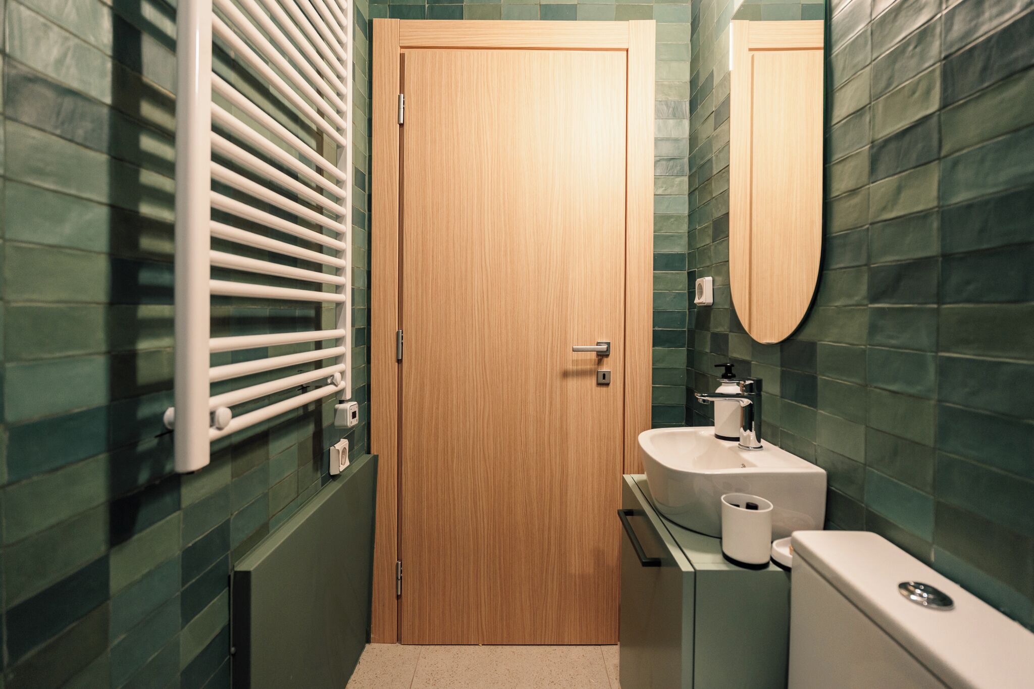 Une salle de bain avec une porte en bois, un lavabo blanc, un miroir et des toilettes.