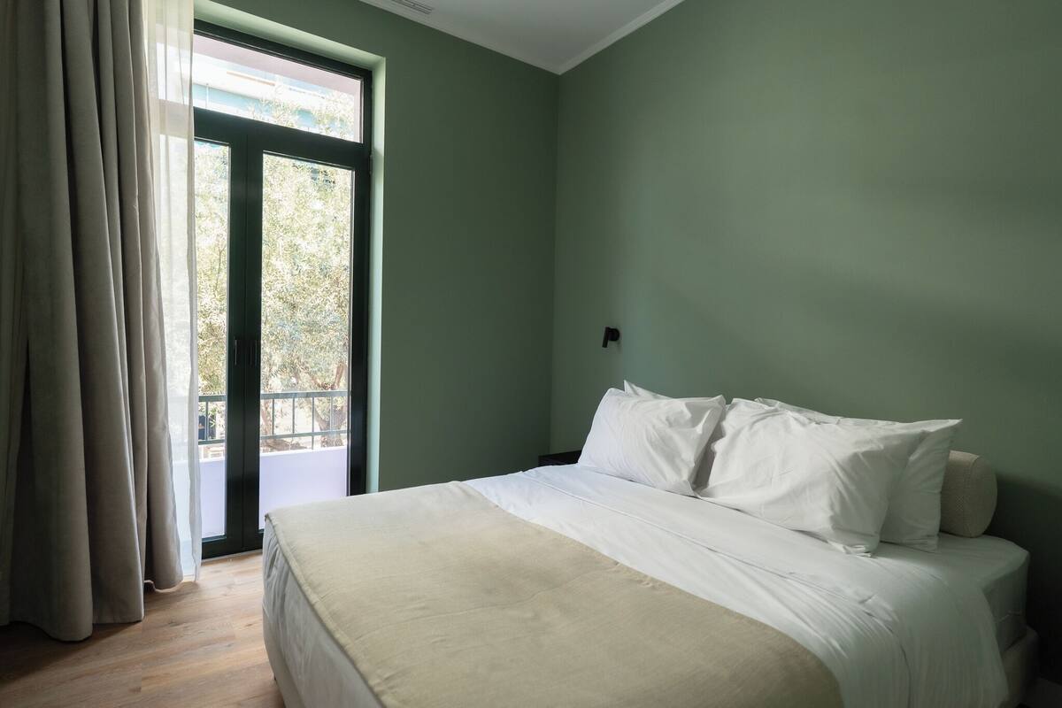 A bedroom with a bed, a window with curtains, and a view of greenery outside.