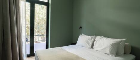A bedroom with a bed, a window with curtains, and a view of greenery outside.