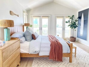 Ein Schlafzimmer mit Bett, Nachttischen, einer Lampe, einer Topfpflanze und Blick ins Freie.