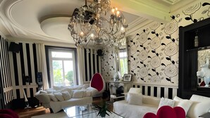 A modern living room with a white sofa, a glass coffee table, and a red chair. There is a chandelier above the table and a black and white patterned wall. - Estate in Saint-pavace Near Le Mans Circuit (Saint-Pavace)