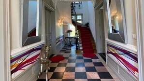 A grand hallway with a checkered floor, a staircase with red carpet, and a decorative ceiling light fixture. - Estate in Saint-pavace Near Le Mans Circuit (Saint-Pavace)