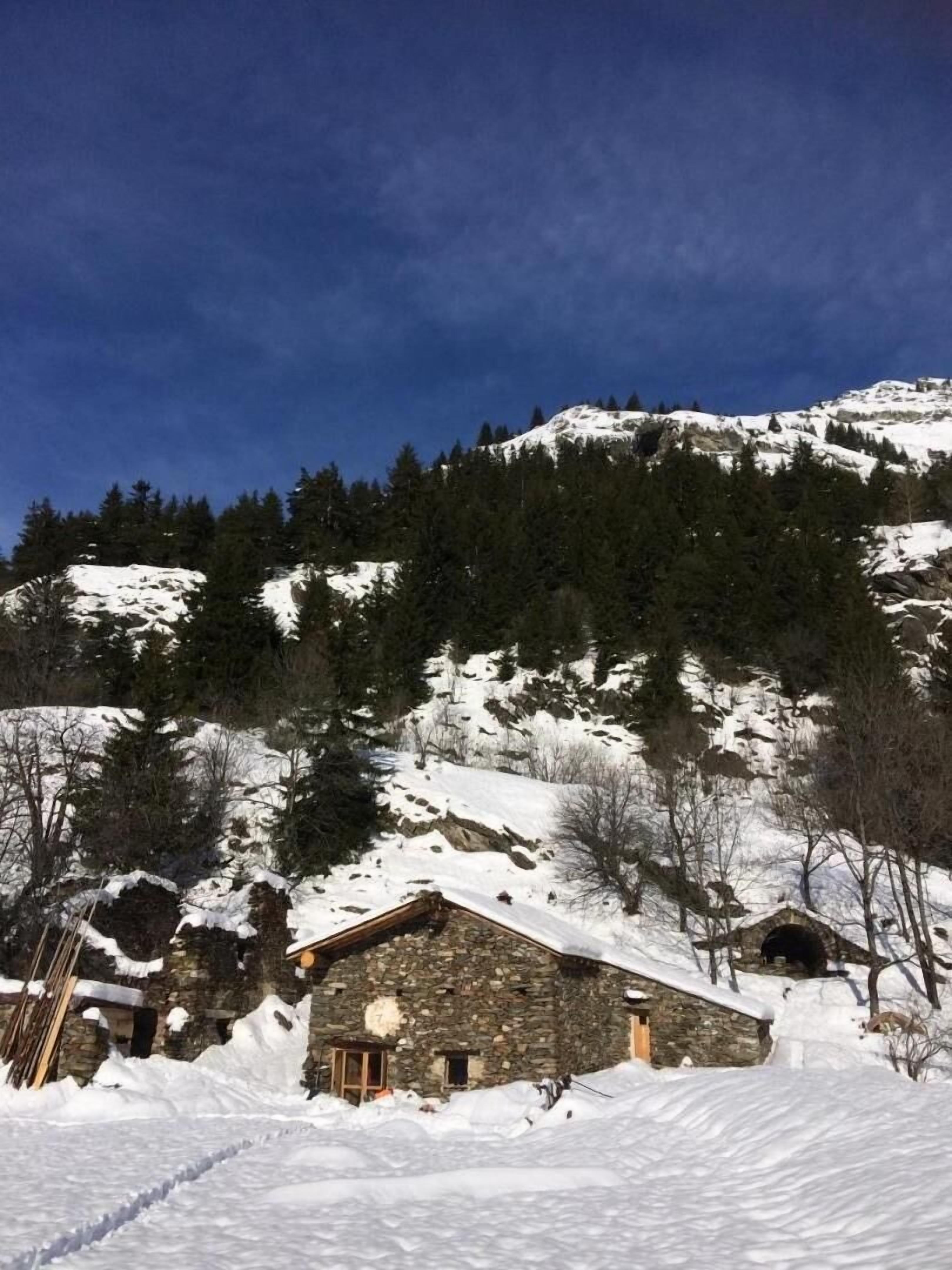 A stone building with a snow-covered roof, surrounded by snow and trees on a mountain.