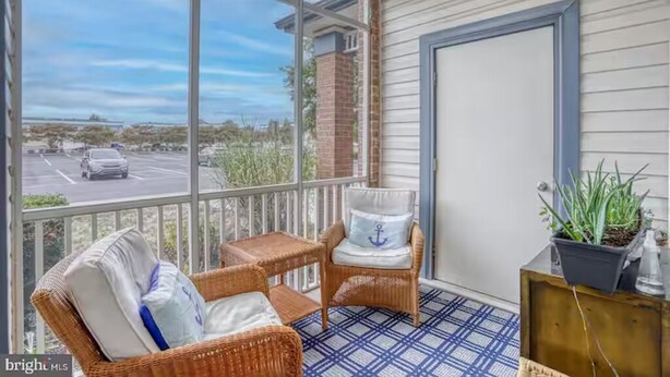 A covered porch with wicker furniture, a potted plant, and a view of a parking lot.