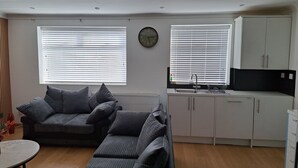 A compact living space with a sofa set, a dining table, a kitchen area with cabinets and a sink, and a clock on the wall. - Grand Apartments Stretford (Stretford)
