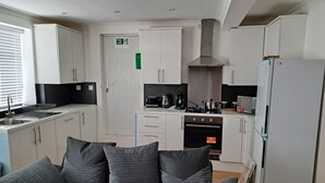 A compact kitchen with white cabinets, a stove, microwave, and a refrigerator. - Grand Apartments Stretford (Stretford)