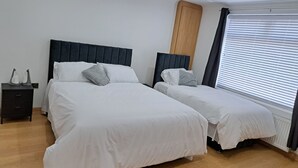 A double bed with a wooden headboard, a bedside table, and a window with blinds. - Grand Apartments Stretford (Stretford)