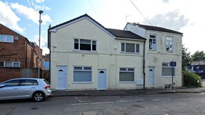 A two-story building with a garage door, a car parked in front, and a street sign indicating a dual carriageway. - Grand Apartments Stretford (Stretford)