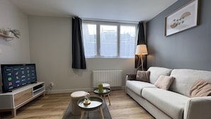 A modern living room with a sofa, a coffee table, a TV, and a window with curtains. - Duplex in Le Mans Near 24 Hours Circuit (Le Mans)