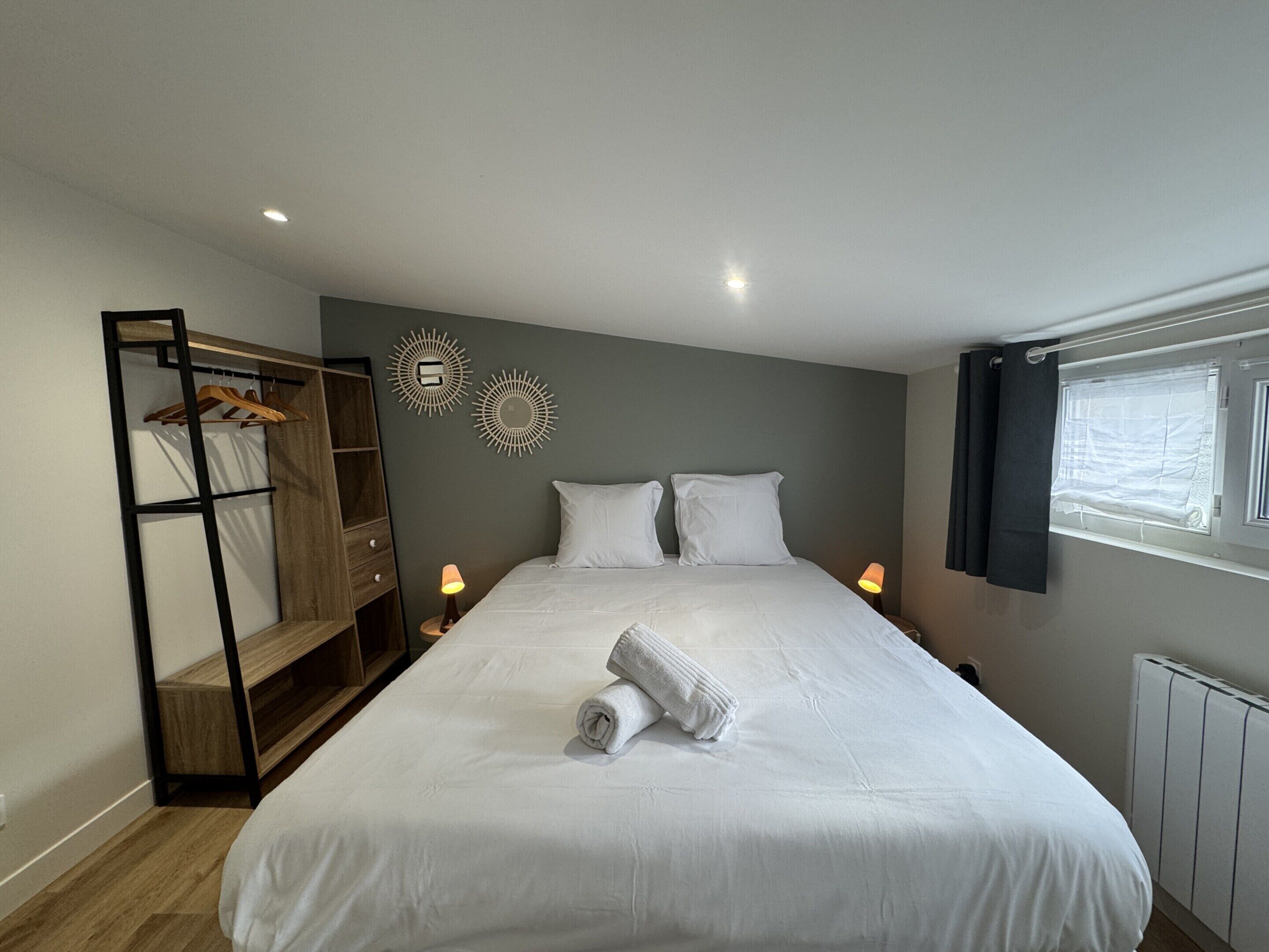 A bedroom with a large bed, a wooden wardrobe, two wall-mounted lamps, and a window with curtains.
