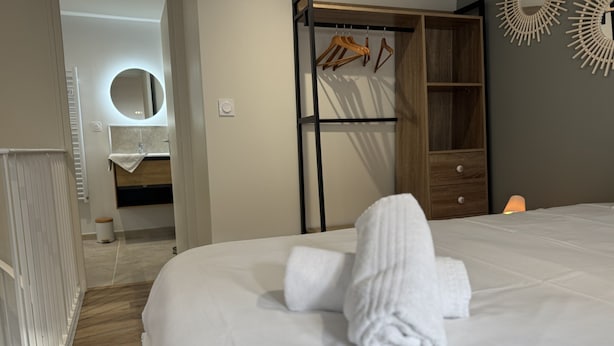 A neatly made bed with a rolled towel, a wooden wardrobe with hanging clothes, and a mirror on the wall. - Duplex in Le Mans Near 24 Hours Circuit (Le Mans)