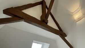 Un dormitorio con techo inclinado, tragaluces, cama, dos mesitas de noche con lámparas y estructura de vigas de madera.