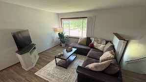 A living room with a sofa, a coffee table, a TV, a lamp, and a window.