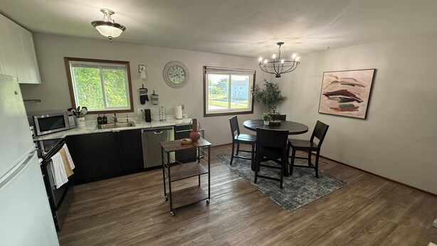 A modern kitchen with a dining area, wooden flooring, and a chandelier.