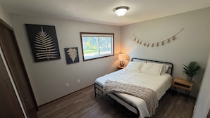A bedroom with a bed, a window, a wall-mounted lamp, and artwork.