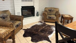 Un salon avec une cheminée, des canapés en cuir, une table basse en bois, un tapis et une petite table en bois.
