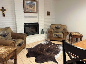 Una sala de estar con chimenea, sofás de cuero, una mesa de centro de madera, una alfombra y una pequeña mesa de madera.