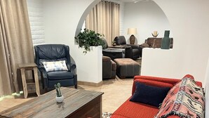 Un salon avec un canapé rouge, une table basse en bois, un fauteuil en cuir noir et un mur en briques blanches.