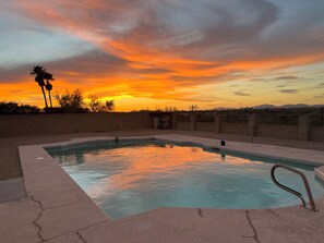 Une piscine avec vue sur le coucher de soleil, entourée d’un mur de briques et de palmiers.