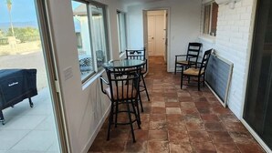 Une pièce spacieuse avec une grande table à manger et des chaises, une porte-fenêtre coulissante donnant sur un espace extérieur, et un mur en briques blanches.