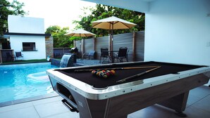 A pool table with balls and cues, a pool, and outdoor seating with umbrellas. - Hacienda los gemelos w/Pool, pool table & Wi-Fi, & beautiful contryside setting. (Ciales)