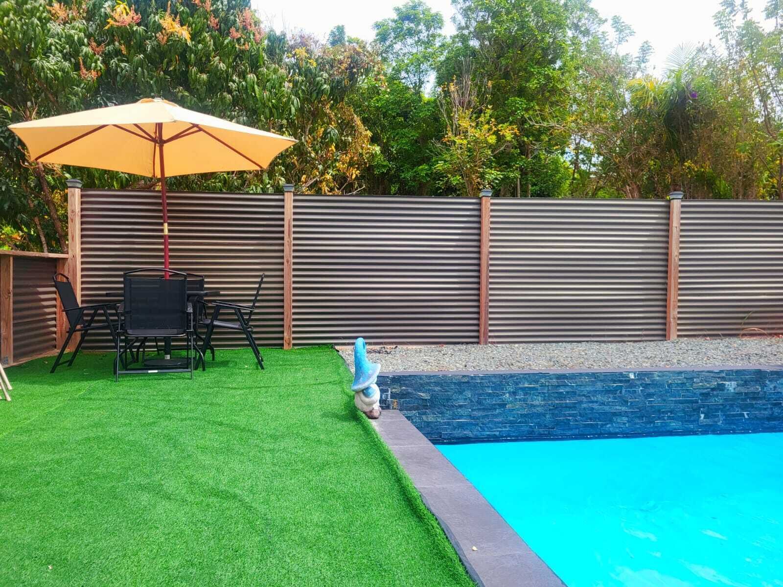 A backyard with artificial grass, a pool, a table with chairs, and a wooden fence.