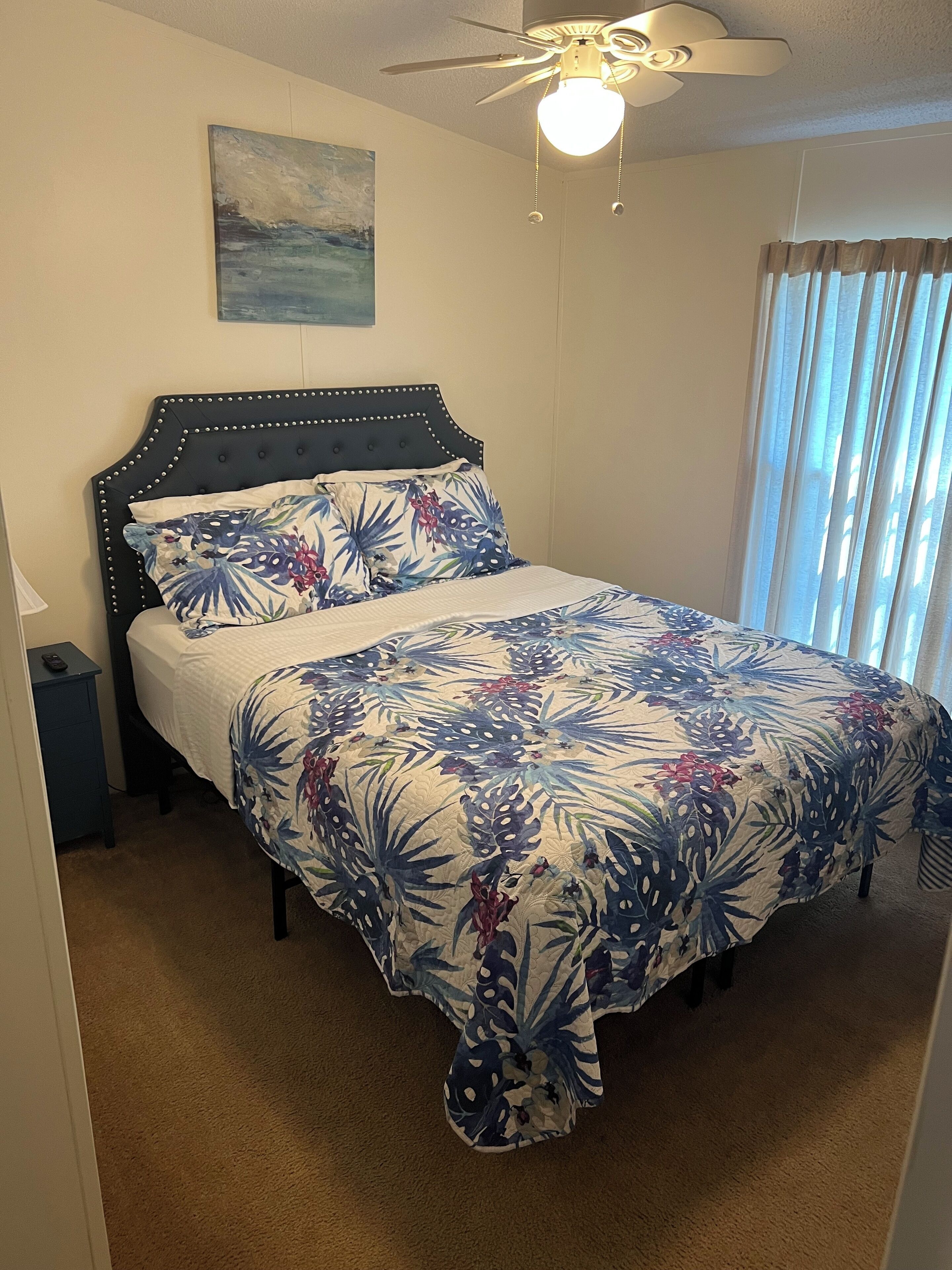 A bedroom with a bed, a ceiling fan, a nightstand, and a window with curtains.