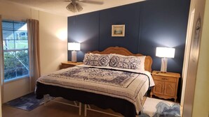 A bedroom with a bed, two bedside tables, a nightstand, a window with curtains, and a ceiling fan. - “Our Lakeside Oasis” is a Cozy 2-bedroom house in charming Okeechobee. (Okeechobee)