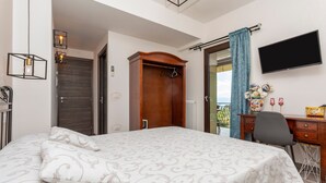 A bedroom with a bed, a wooden wardrobe, a desk with a chair, a TV, and a balcony with a view. - 'Executive Suite' room with private balcony, sea view, Wi-Fi and air conditioning (Savoca)