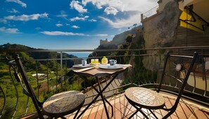 Un balcón con una mesa lista para dos personas, con vistas a un paisaje pintoresco de colinas y cielo despejado.
