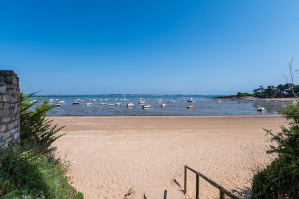 A beach with boats, a stone wall, and a wooden railing.