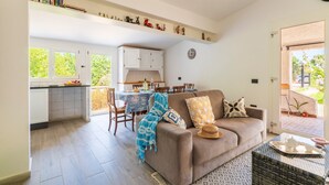 A living room with a sofa, a dining table, and a kitchen area with cabinets. - Holiday Home 'Dammar' with Mountain View, Wi-Fi and Air Conditioning (Tertenìa)