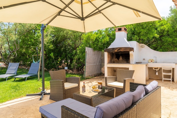 Un patio al aire libre con mobiliario de mimbre, una mesa de vidrio y una zona de barbacoa.
