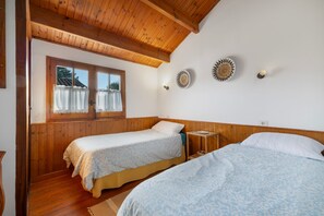 Une chambre avec deux lits, des murs en bois, une fenêtre avec des rideaux et des luminaires fixés au mur.