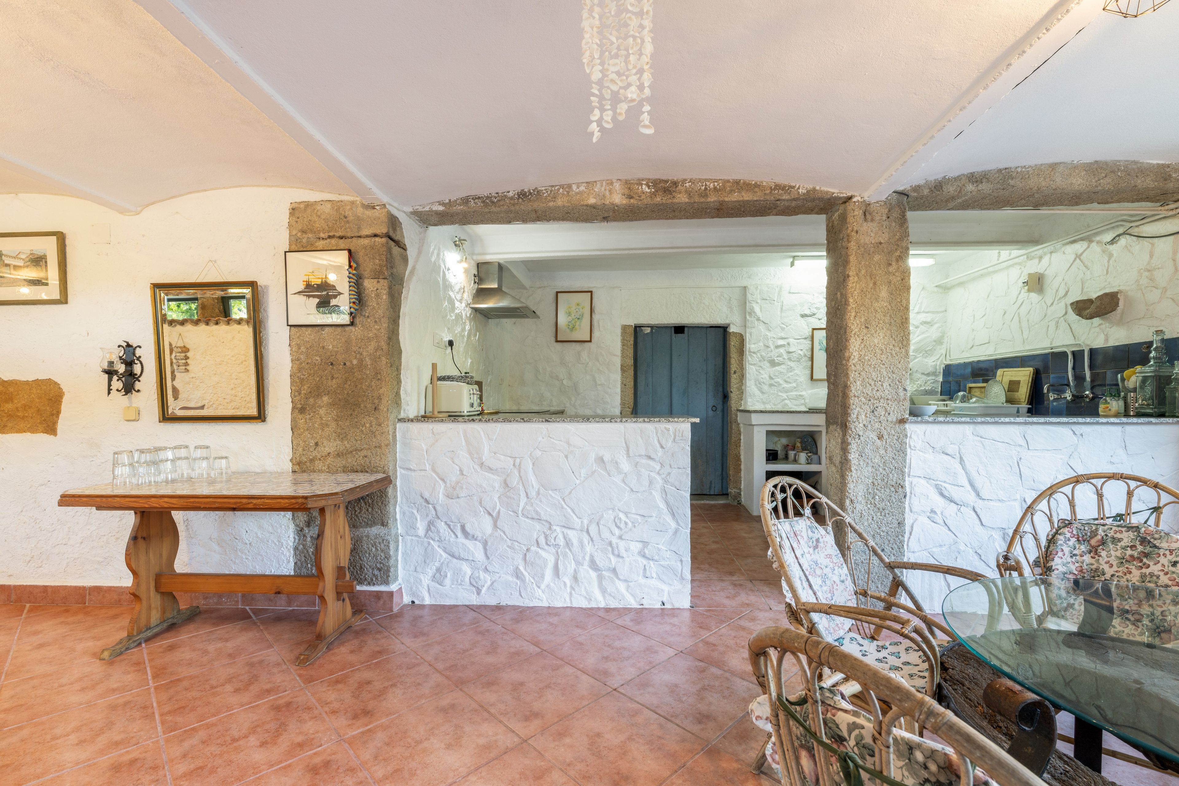 Una cocina amplia con una isla central, paredes de piedra rústica y un comedor con mesa de madera y sillas de mimbre.