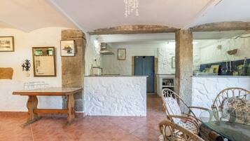 Una cocina amplia con una isla central, paredes de piedra rústica y un comedor con mesa de madera y sillas de mimbre.